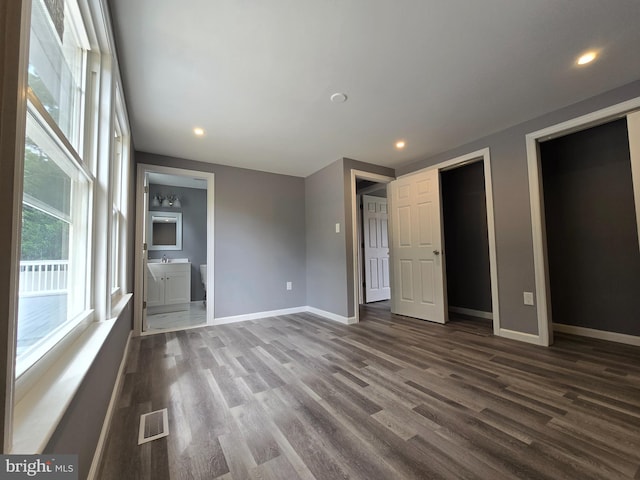 unfurnished bedroom with ensuite bathroom and dark hardwood / wood-style flooring