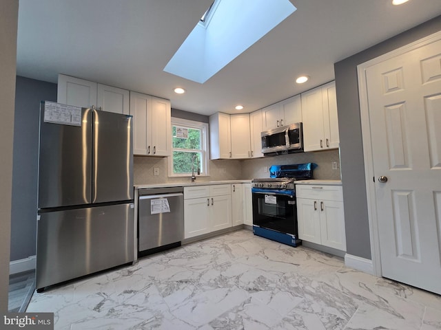 kitchen featuring a skylight, appliances with stainless steel finishes, white cabinets, and decorative backsplash