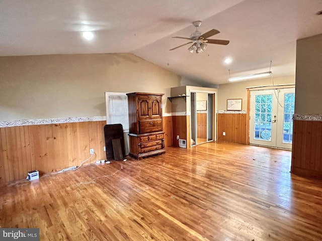 unfurnished living room featuring vaulted ceiling, hardwood / wood-style floors, wood walls, and french doors