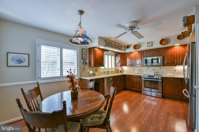 interior space with hanging light fixtures, wood-type flooring, decorative backsplash, ceiling fan, and appliances with stainless steel finishes