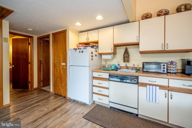 kitchen featuring white appliances, sink, light hardwood / wood-style floors, a textured ceiling, and cream cabinets