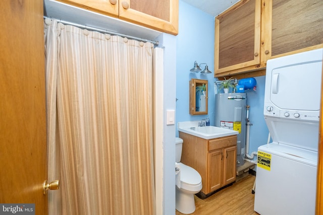 bathroom featuring stacked washer / drying machine, toilet, vanity, hardwood / wood-style floors, and water heater