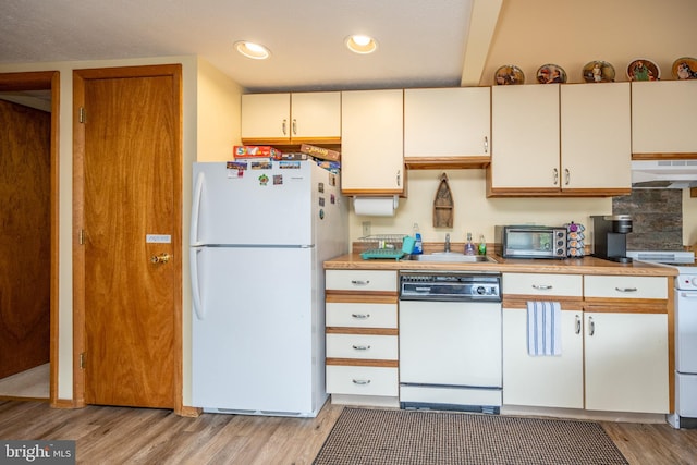 kitchen with white appliances, wall chimney range hood, cream cabinets, light hardwood / wood-style floors, and sink