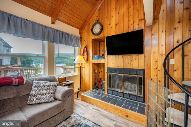 living room featuring vaulted ceiling with beams, wood walls, a tile fireplace, and hardwood / wood-style floors