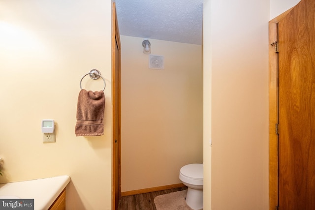 bathroom featuring wood-type flooring, toilet, vanity, and a textured ceiling