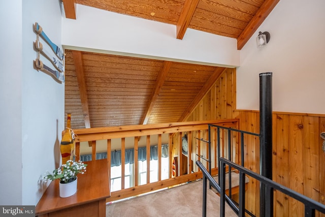 hall featuring carpet floors, lofted ceiling with beams, wooden walls, and wood ceiling