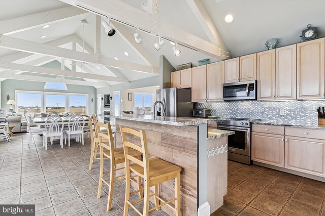 kitchen with appliances with stainless steel finishes, backsplash, an island with sink, tile patterned floors, and track lighting