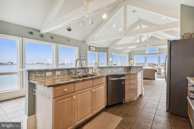 kitchen featuring vaulted ceiling with beams, a kitchen island with sink, stainless steel appliances, a water view, and a sink