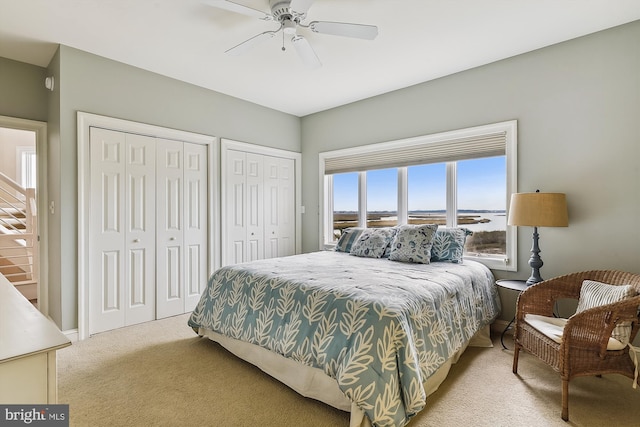 bedroom with light carpet, ceiling fan, a water view, and two closets