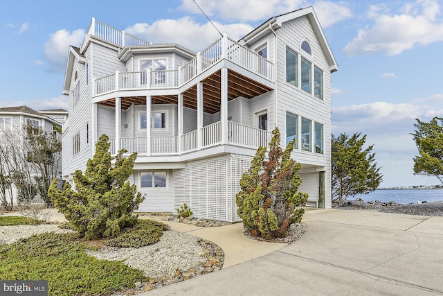 view of front facade with a garage, a water view, driveway, and a balcony