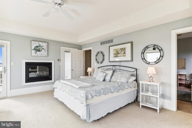 carpeted bedroom with a ceiling fan, a glass covered fireplace, visible vents, and baseboards