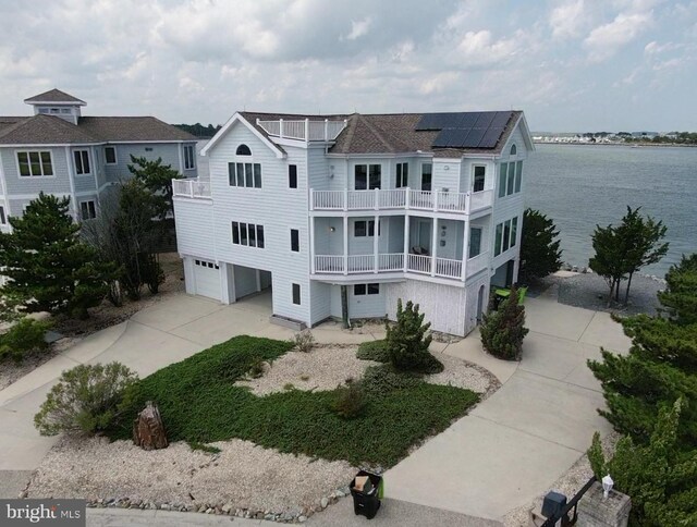 rear view of house featuring a garage, solar panels, a balcony, and a water view