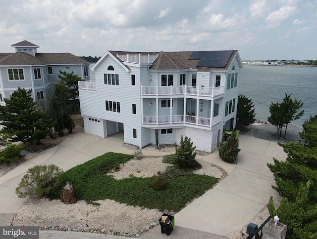 view of front of home with solar panels, a water view, a balcony, a garage, and driveway