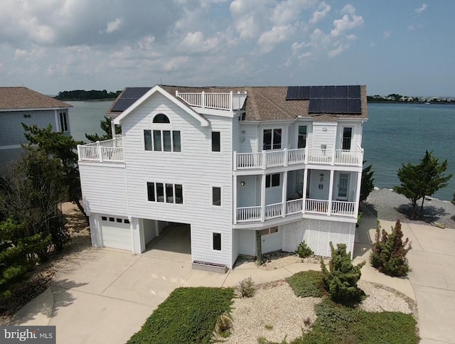 view of front facade with a balcony, a water view, roof mounted solar panels, and concrete driveway