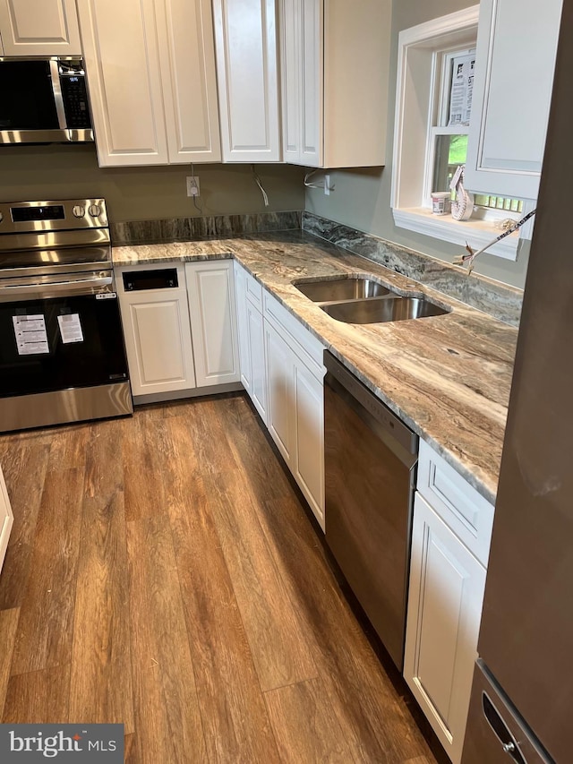 kitchen featuring appliances with stainless steel finishes, light stone counters, white cabinets, wood-type flooring, and sink