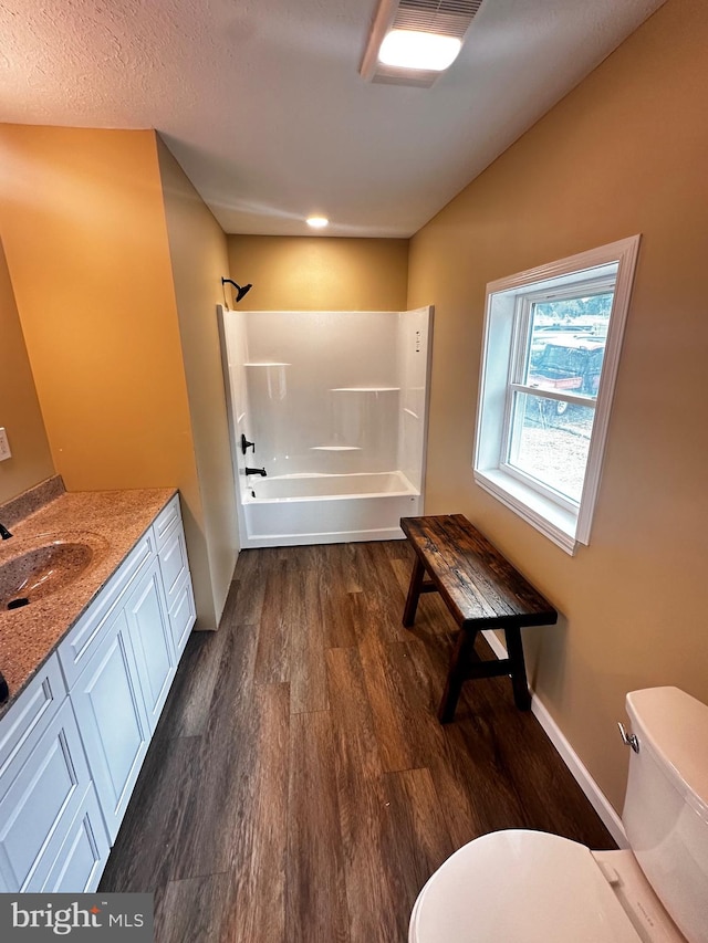 full bathroom featuring bathing tub / shower combination, vanity, a textured ceiling, hardwood / wood-style floors, and toilet