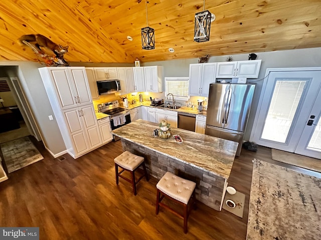 kitchen featuring appliances with stainless steel finishes, white cabinets, light stone countertops, lofted ceiling, and decorative light fixtures