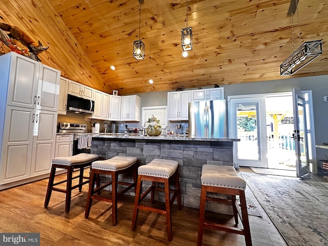 kitchen with appliances with stainless steel finishes, light hardwood / wood-style floors, white cabinetry, and pendant lighting