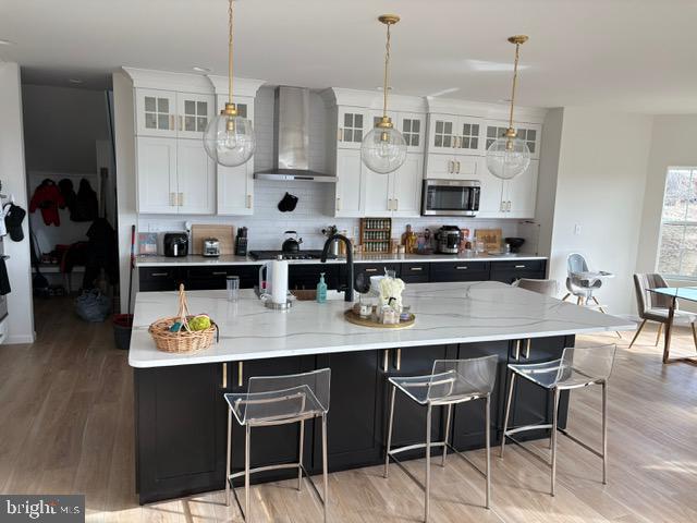 kitchen featuring hanging light fixtures, wall chimney range hood, a large island, decorative backsplash, and white cabinets