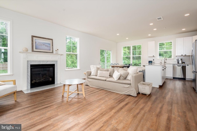 living room with a high end fireplace, sink, light hardwood / wood-style flooring, and plenty of natural light