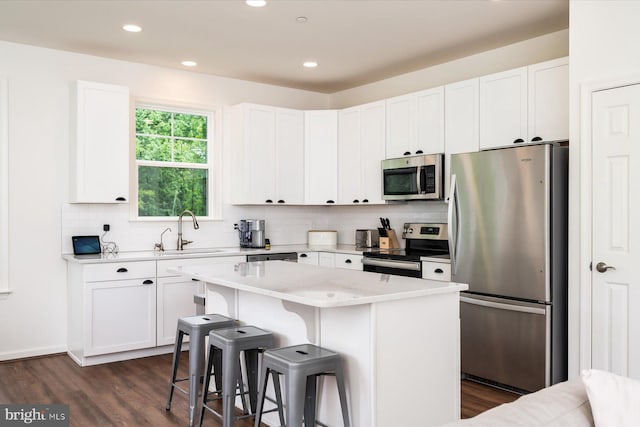 kitchen with sink, appliances with stainless steel finishes, white cabinetry, a center island, and a kitchen bar