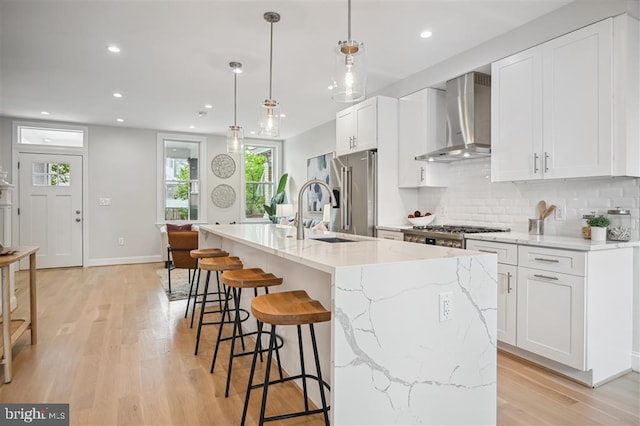 kitchen featuring light hardwood / wood-style floors, a kitchen island with sink, light stone countertops, and wall chimney exhaust hood