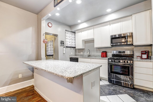 kitchen with sink, a breakfast bar area, white cabinetry, stainless steel appliances, and light stone counters