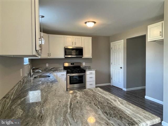 kitchen featuring appliances with stainless steel finishes, white cabinetry, sink, dark hardwood / wood-style flooring, and light stone counters