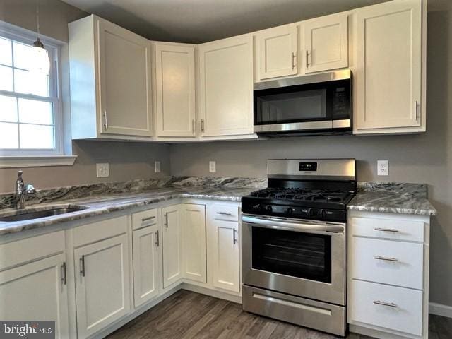 kitchen featuring sink, appliances with stainless steel finishes, white cabinetry, dark hardwood / wood-style floors, and light stone countertops