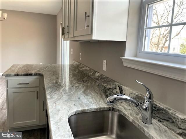 details with gray cabinetry, sink, a notable chandelier, and light stone countertops