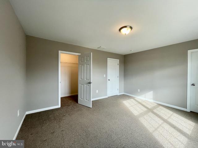 unfurnished bedroom featuring a walk in closet, carpet floors, and a closet