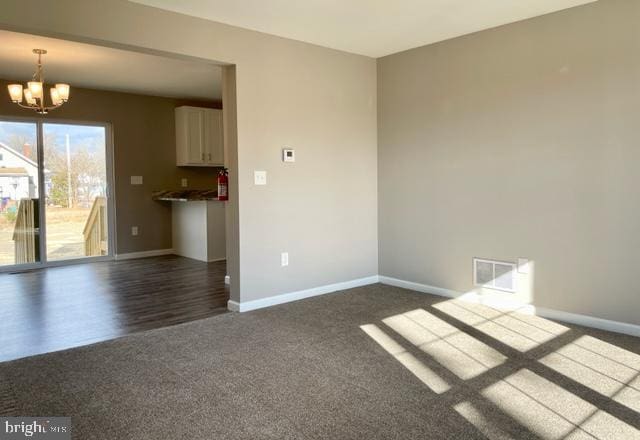 unfurnished living room featuring dark colored carpet and a notable chandelier