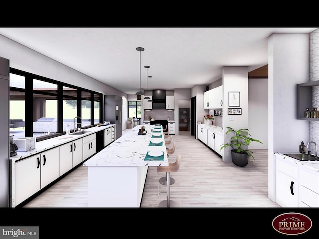 kitchen with light wood-type flooring, white cabinets, a kitchen island, light stone countertops, and decorative light fixtures