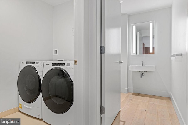 laundry room featuring separate washer and dryer, sink, and light hardwood / wood-style floors