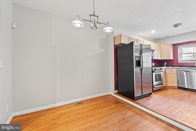 kitchen with light brown cabinetry, decorative light fixtures, stainless steel appliances, and light wood-type flooring