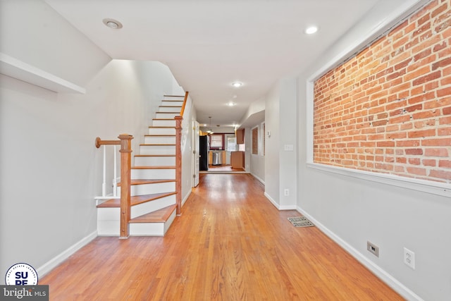 corridor with light hardwood / wood-style flooring and brick wall