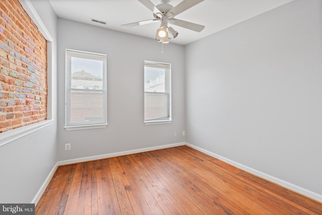 spare room with ceiling fan, hardwood / wood-style floors, and brick wall