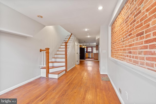 hallway with brick wall and hardwood / wood-style flooring