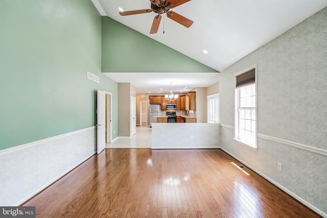 unfurnished living room with ceiling fan with notable chandelier, vaulted ceiling, and light hardwood / wood-style floors