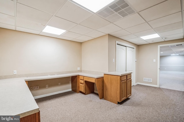 unfurnished office with built in desk, light colored carpet, and a paneled ceiling