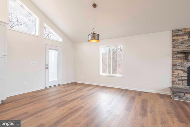 unfurnished dining area with lofted ceiling, a stone fireplace, dark wood finished floors, and baseboards