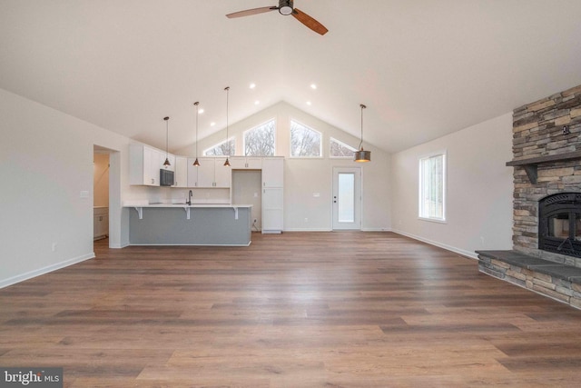 unfurnished living room with light wood-style floors, high vaulted ceiling, a sink, and a stone fireplace