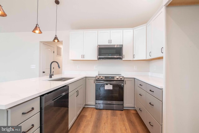 kitchen featuring decorative light fixtures, stainless steel appliances, gray cabinetry, white cabinets, and a sink