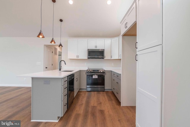 kitchen with stainless steel appliances, light countertops, hanging light fixtures, a sink, and a peninsula