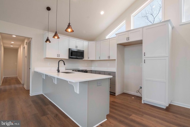 kitchen with a peninsula, white cabinets, light countertops, stainless steel microwave, and decorative light fixtures