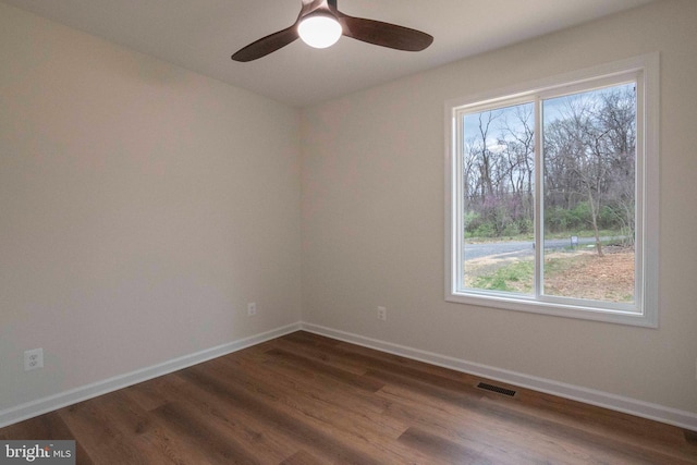 spare room featuring dark wood-type flooring, a ceiling fan, visible vents, and baseboards