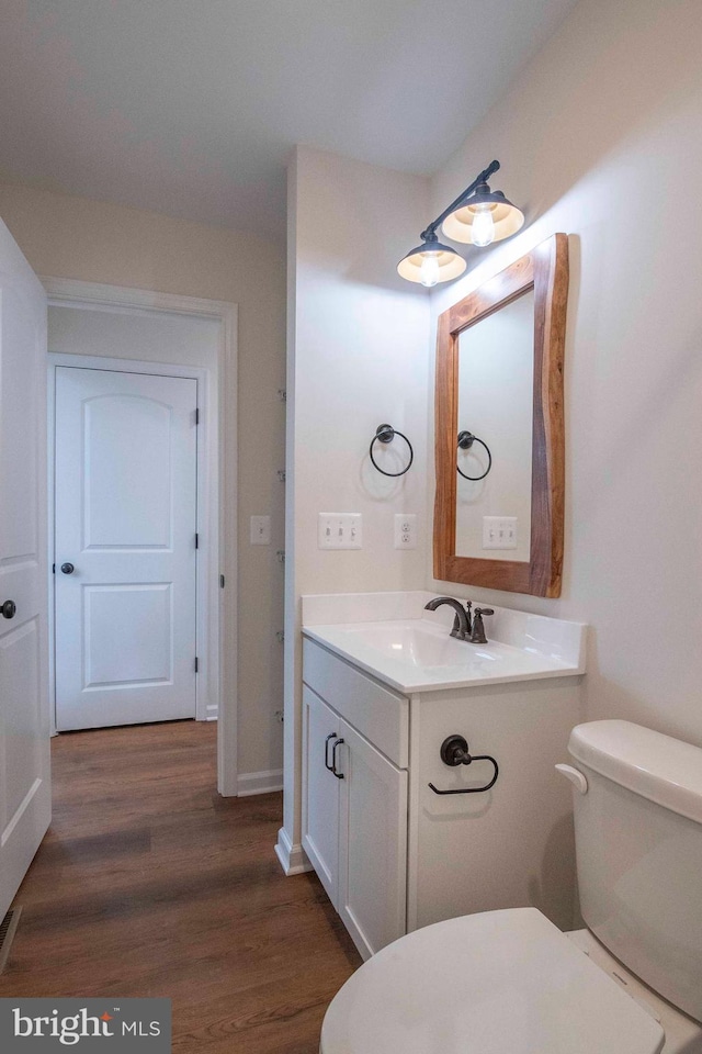 half bathroom with toilet, wood finished floors, and vanity