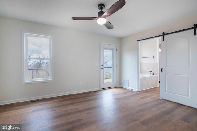 spare room with dark wood-style floors, visible vents, a barn door, a ceiling fan, and baseboards