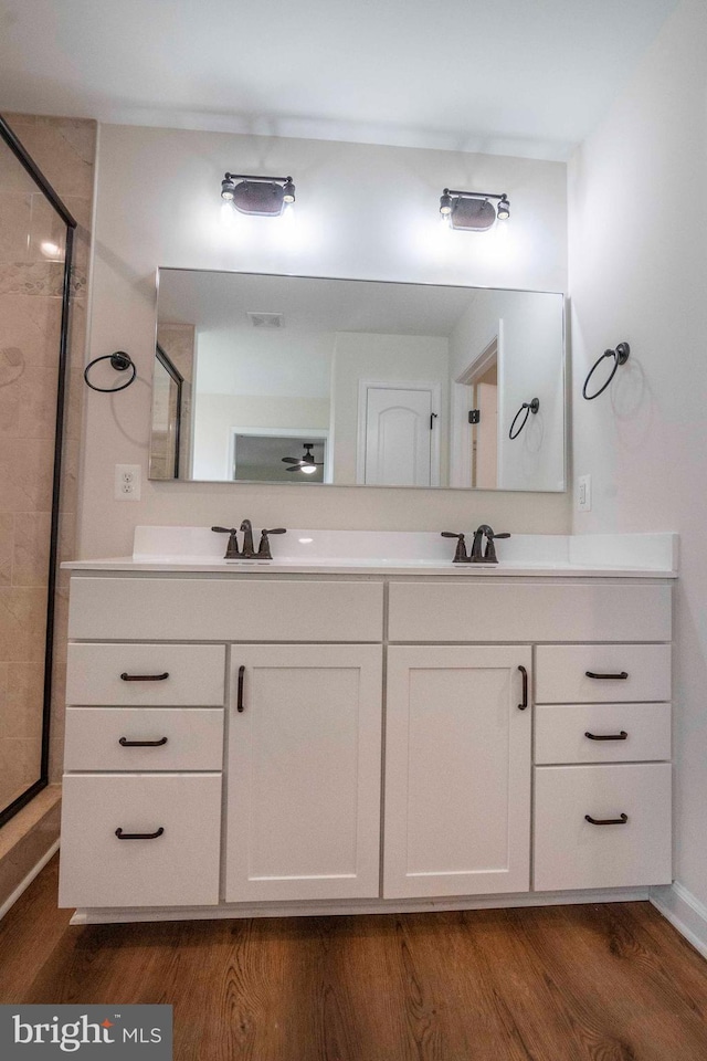 full bathroom with a sink, wood finished floors, visible vents, double vanity, and a stall shower