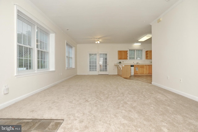 unfurnished living room with plenty of natural light, ceiling fan, light colored carpet, and ornamental molding